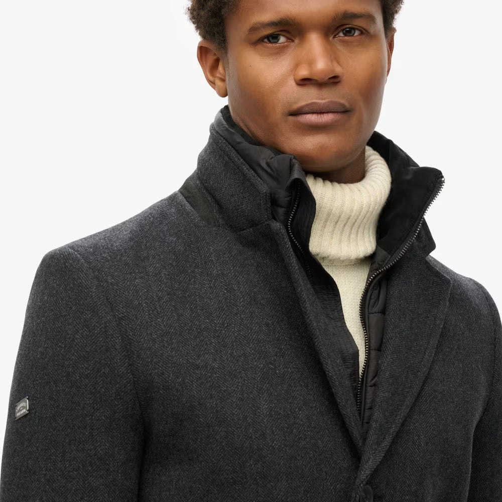 Man wearing a black pea coat over a white turtleneck on a light gray background
