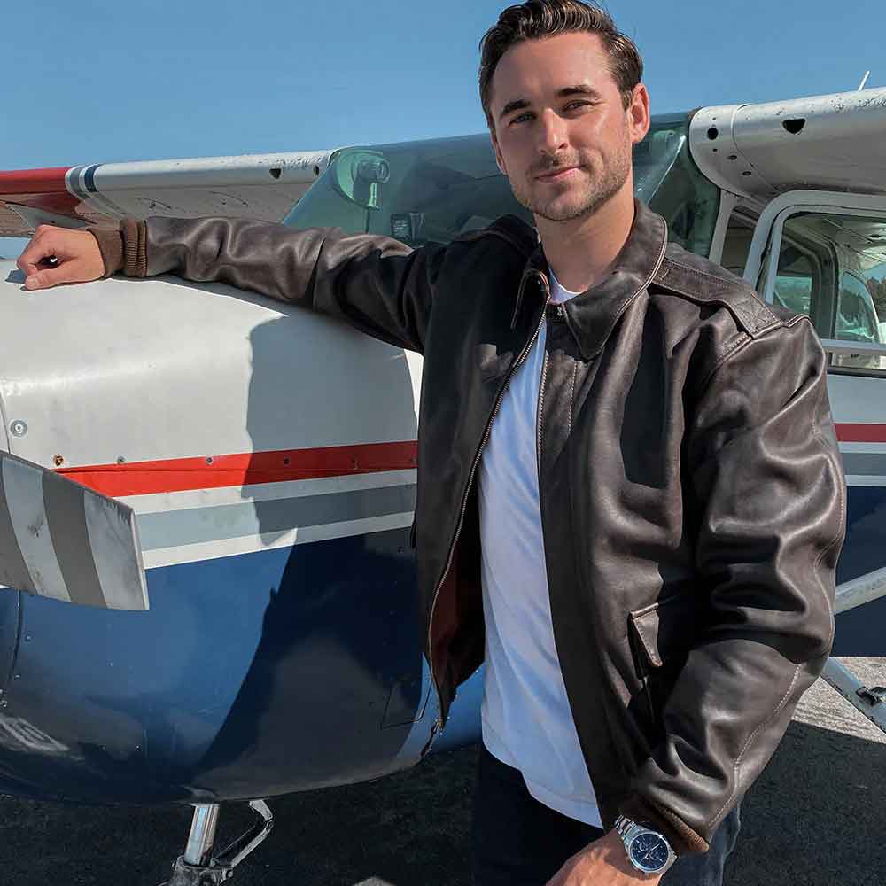 Man in a leather jacket standing next to a small airplane