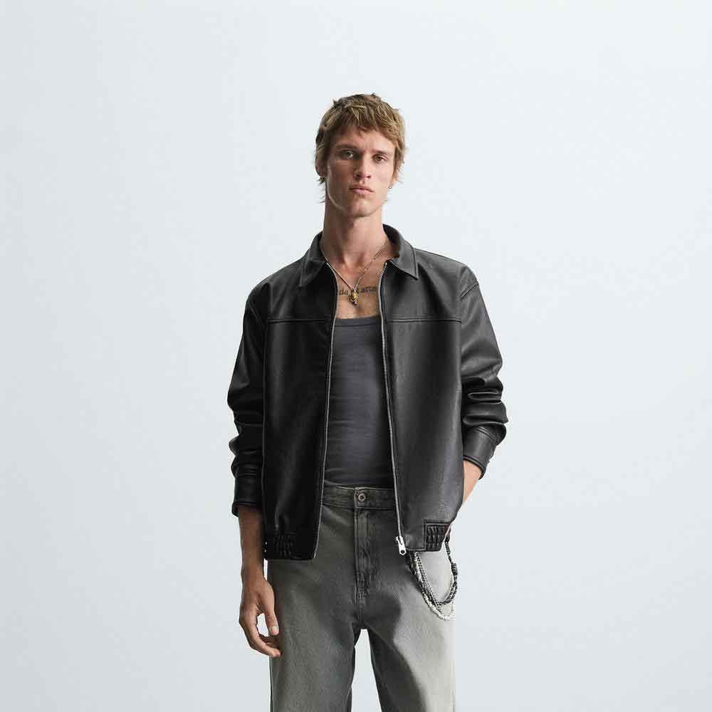 Man wearing a black leather jacket and gray pants against a white background